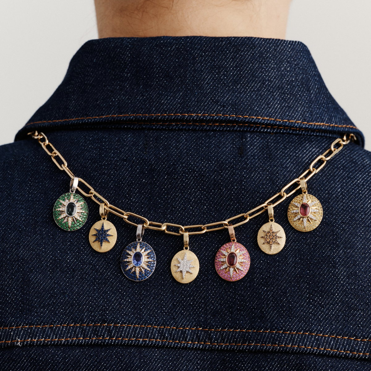 Gold chain necklace with seven celestial gemstone pendants featuring blue sapphires, pink tourmalines, and diamonds on denim collar