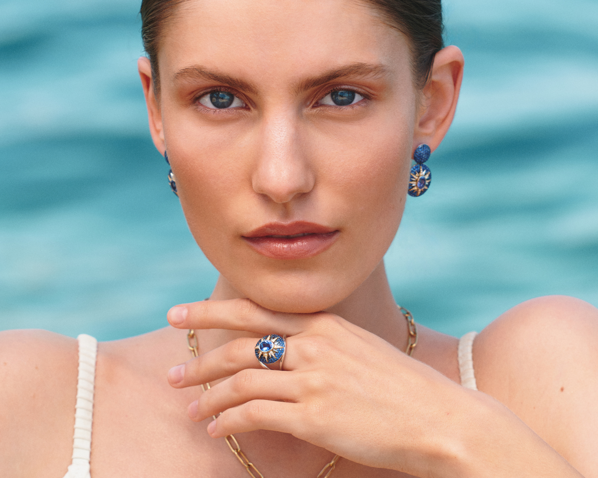 Woman wearing Raphaëlle Coqblin Paris Crush Nova blue sapphire star ring and matching earrings by the sea